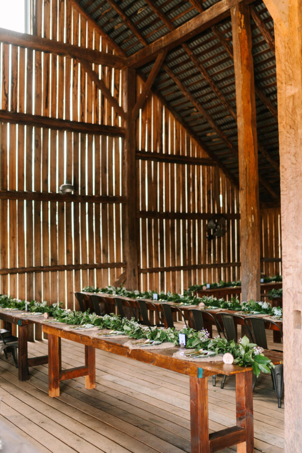 Barn Reception with Long Farm Tables and Greenery – Canaan Springs Rustic barn interior at Canaan Springs featuring long handmade farm tables decorated with lush greenery for a wedding reception in Northern Virginia near Winchester