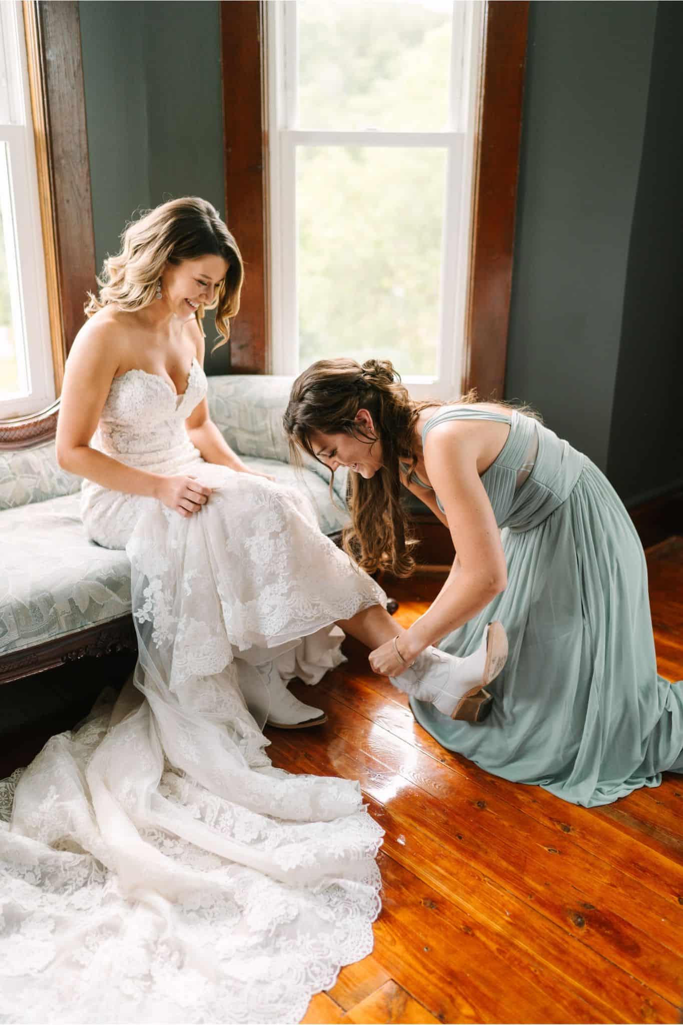 Maid of honor helping bride put on iconic white cowboy boots in the farmhouse Airbnb at Canaan Springs, a Northern VA farm wedding venue near Winchester