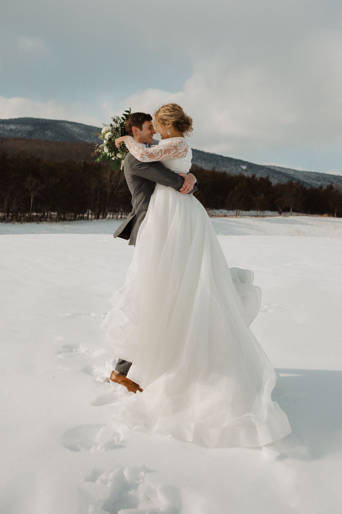 Groom lifting bride in a snowy field with Blue Ridge Mountain backdrop during a winter wedding at Canaan Springs, a rustic farm wedding venue in Northern Virginia