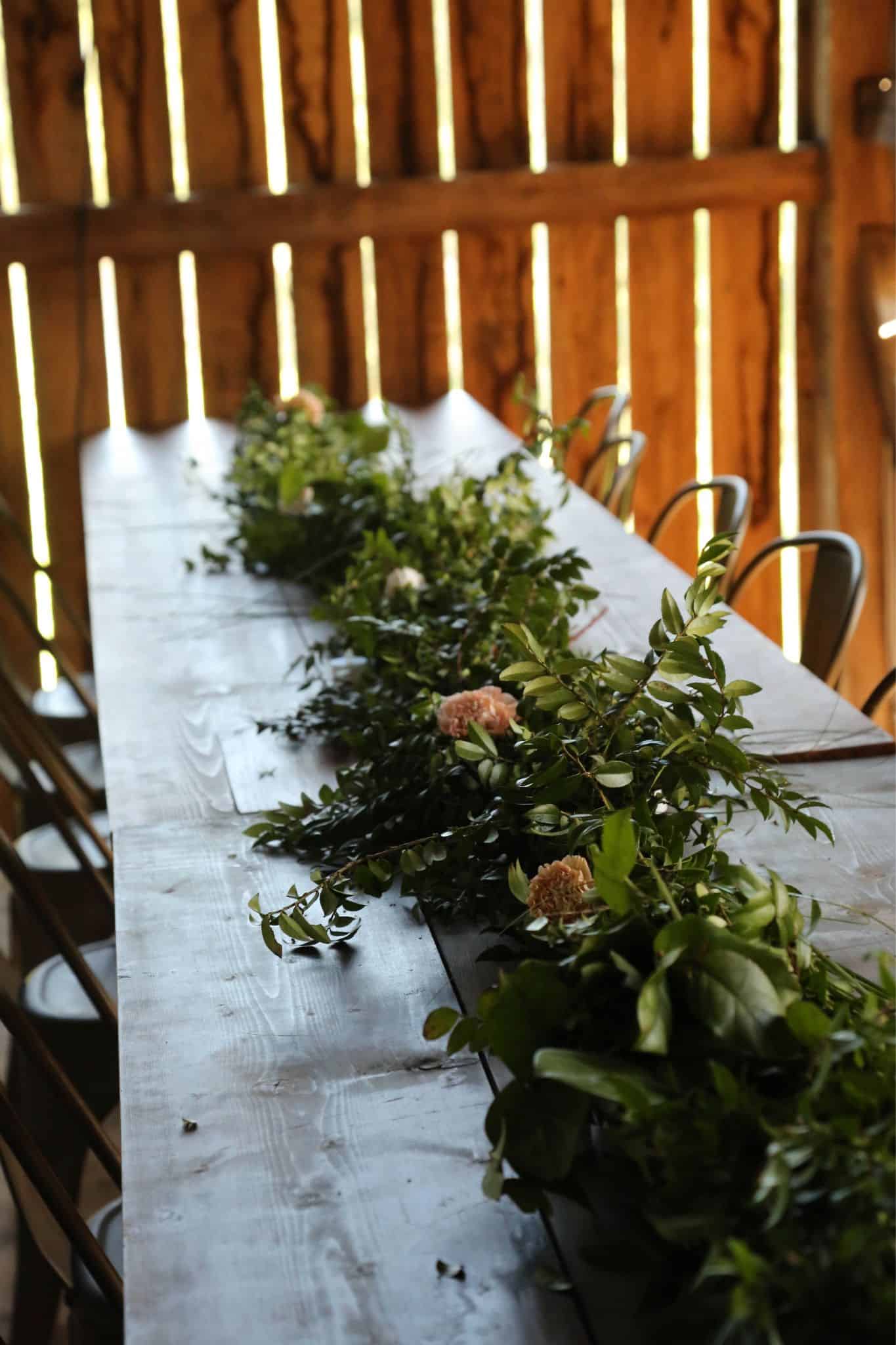 Long handmade wooden farm table at Canaan Springs decorated with lush greenery runner and elegant place settings, ready for wedding reception at this Northern Virginia farm venue