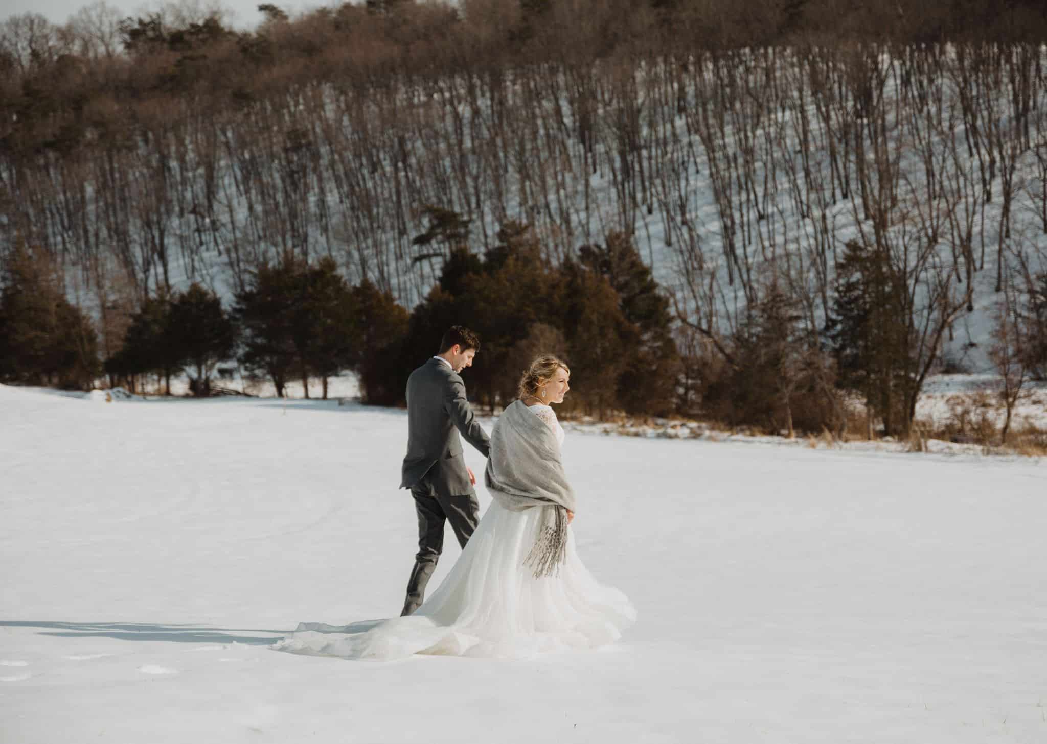 Couple walking away through a snowy field with trees in the background at Canaan Springs, a Northern VA area farm wedding venue near Winchester, VA and the Winchester area