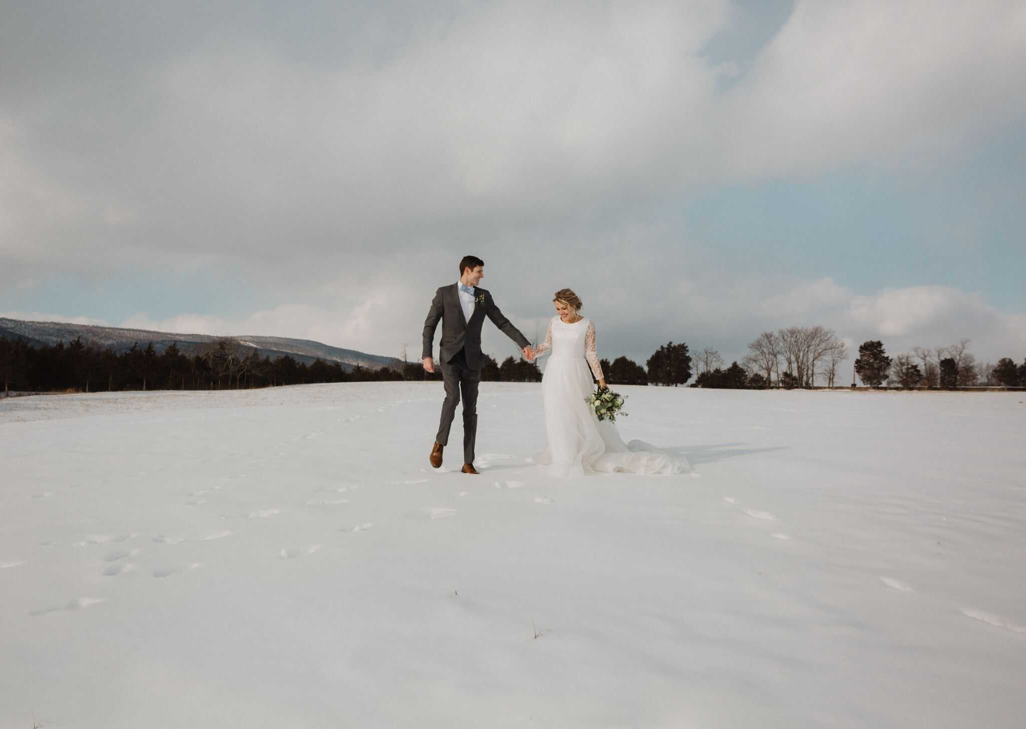 Just married couple walking through snowy fields on hilltops at Canaan Springs, a Northern VA area farm wedding venue near Winchester, VA and the Winchester area