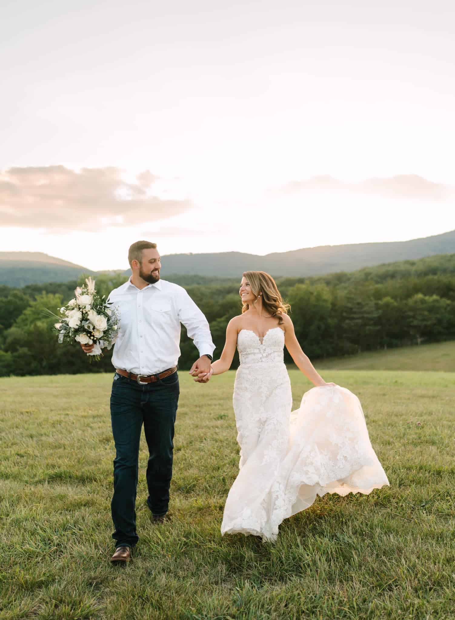 Just married bride and groom holding hands walking on a hilltop with mountain views during a summer evening at Canaan Springs wedding venue in Northern Virginia