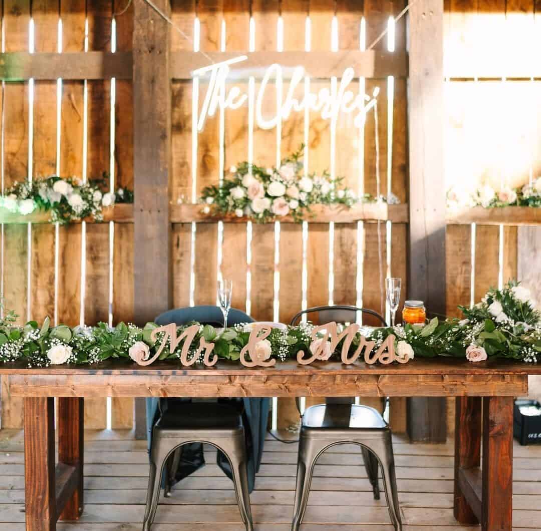 Lit-up custom name sign displaying newlyweds’ last name on barn wall above handmade farm table decorated for bride and groom at Canaan Springs wedding venue in Northern Virginia