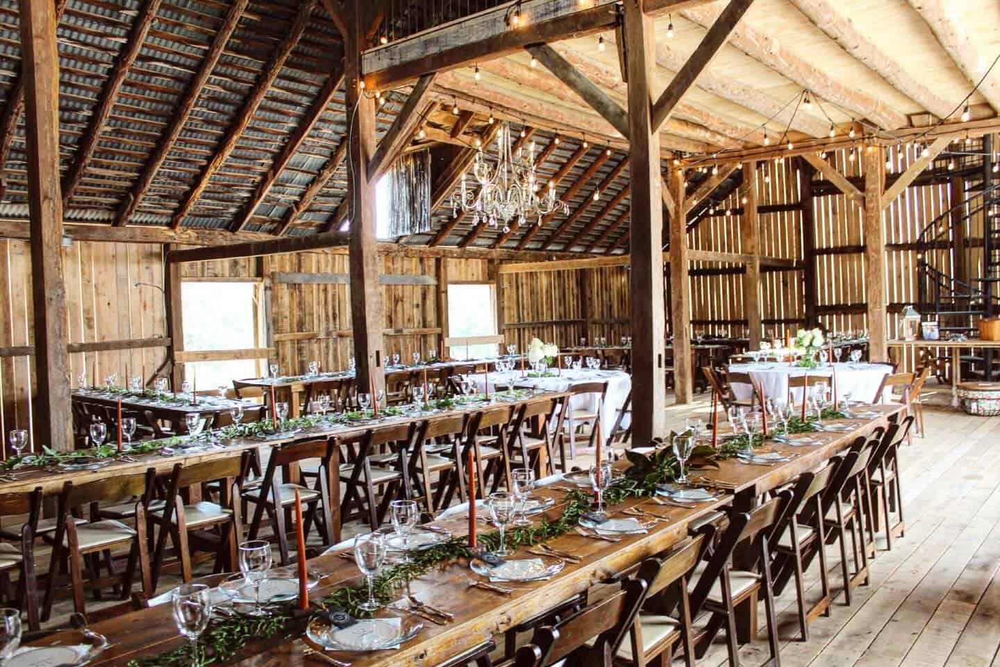 Canaan Springs barn set up for wedding reception with handmade farm tables, wooden chairs, and glowing string lights in Northern Virginia near Winchester