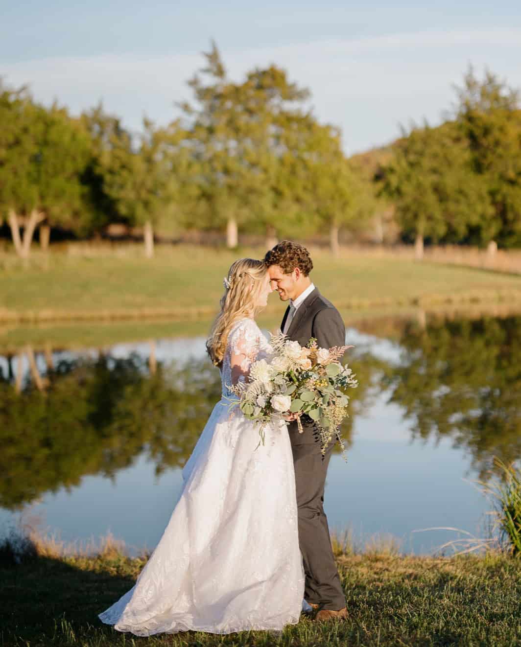 Bride and groom just married posing lovingly in front of a peaceful pond at Canaan Springs, a scenic Northern Virginia farm wedding venue.
