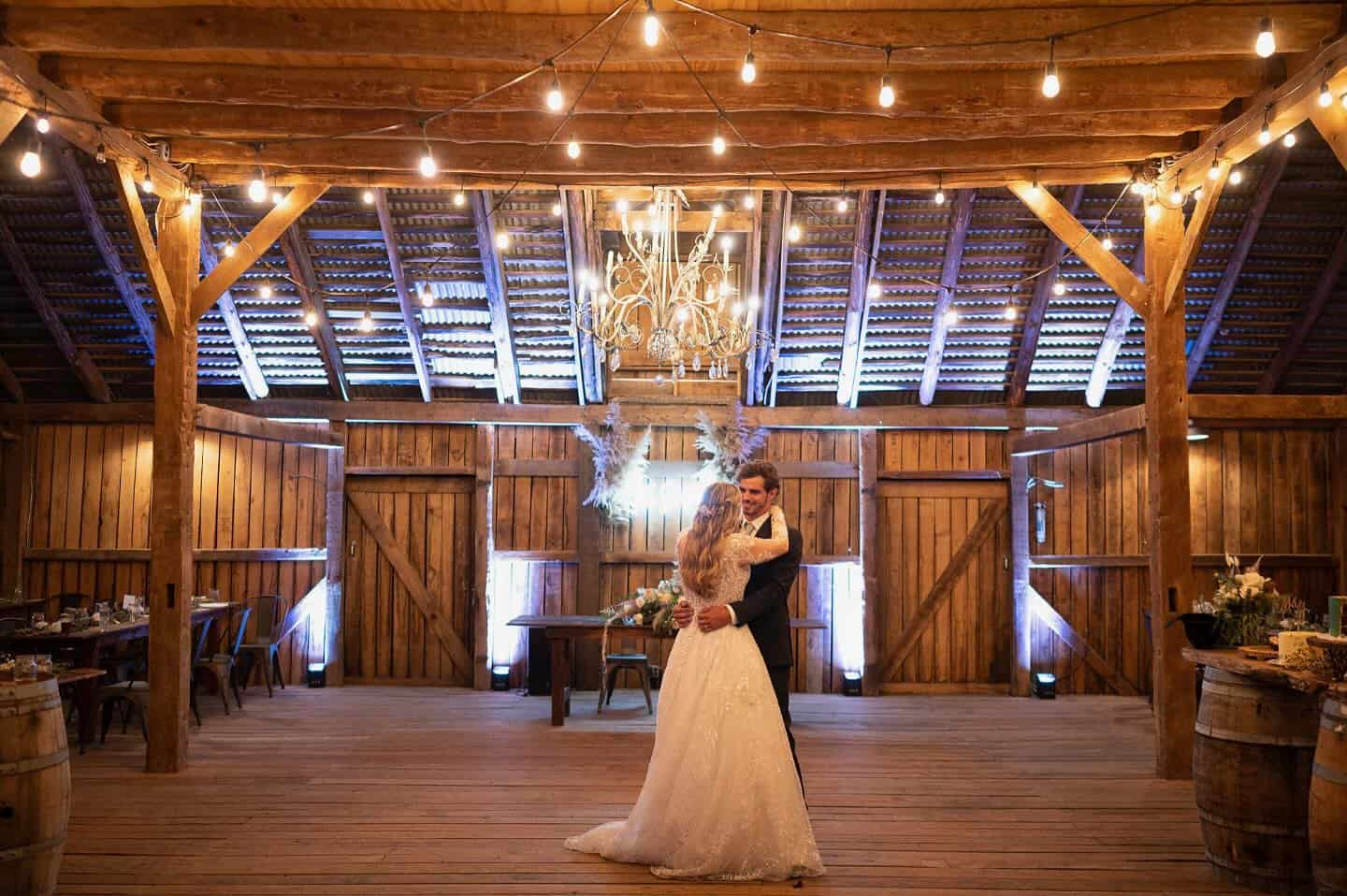 Bride and groom’s first dance under string lights and chandeliers inside the restored barn at Canaan Springs, a romantic Northern VA wedding venue.