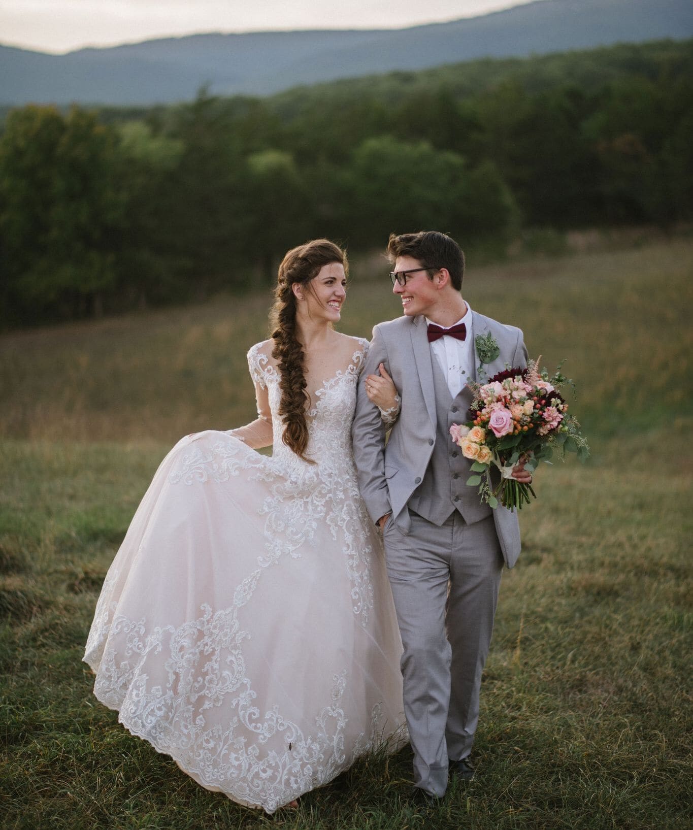 Just married couple walking and smiling at each other on a hilltop at sunset, surrounded by vibrant flowers, bride wearing a lace wedding dress at Canaan Springs, a Northern Virginia farm wedding venue