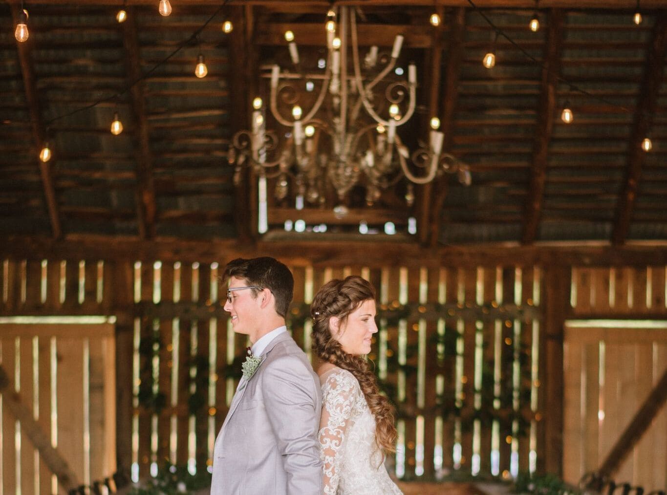 Couple’s first look back-to-back in the barn at Canaan Springs, surrounded by elegant greenery and glowing string lights at this Northern Virginia farm wedding venue