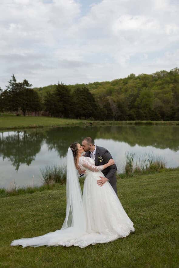 Bride and groom share a kiss beside the peaceful pond at Canaan Springs, a rustic farm wedding venue in Northern Virginia