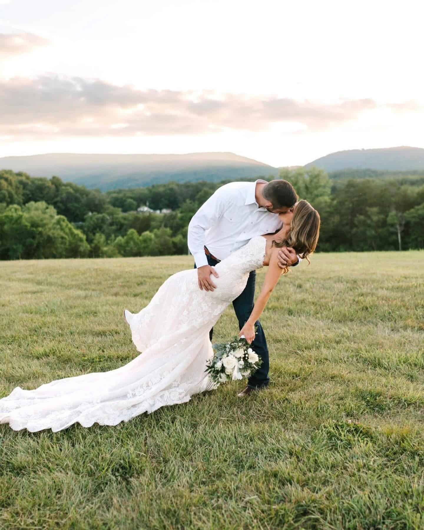 Groom dips and kisses bride on a hill at sunset with Blue Ridge Mountain views at Canaan Springs, a scenic Winchester wedding venue.