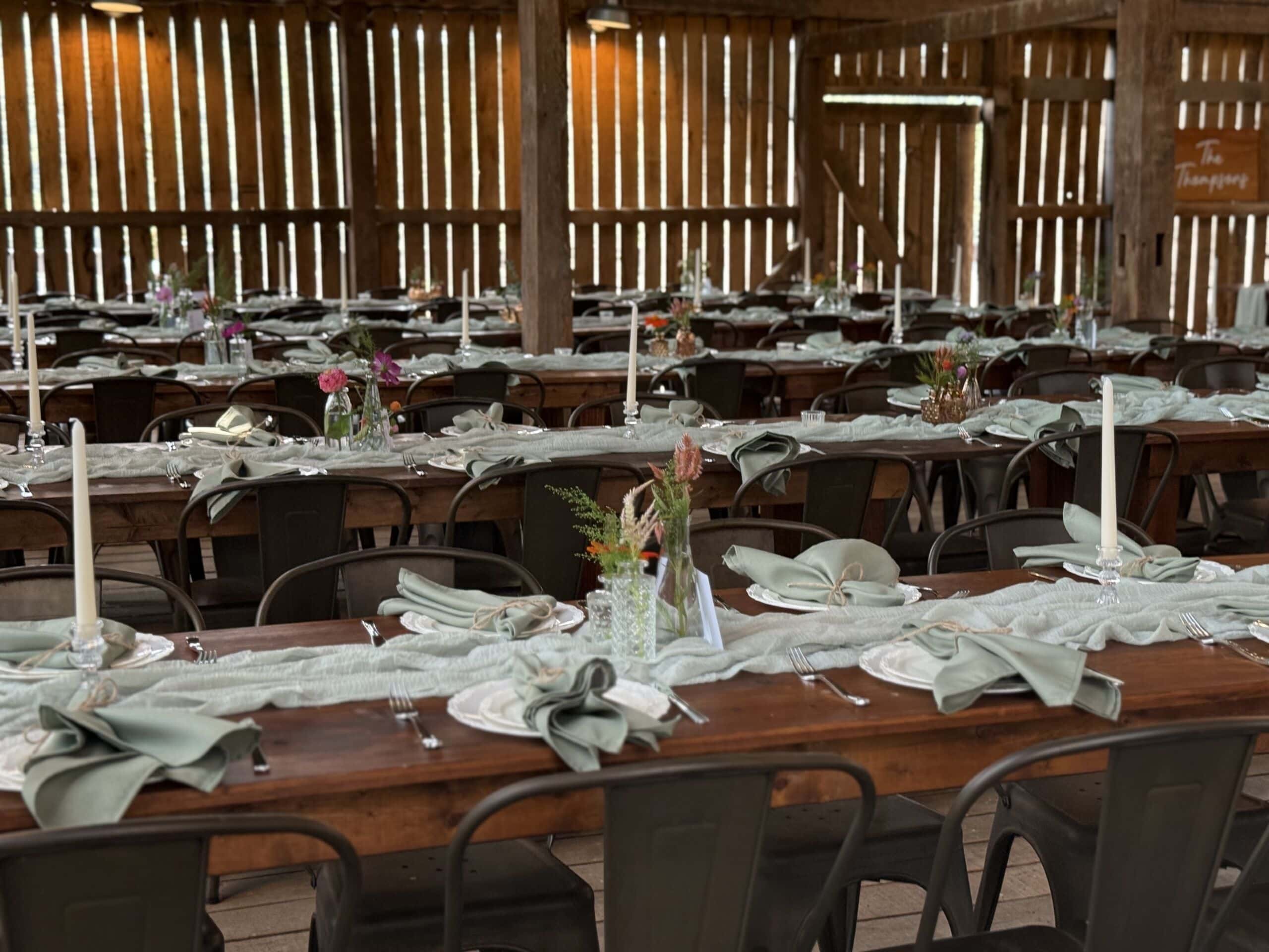 Close-up of long farm tables with green fabric runners decorated for a rustic wedding reception inside the barn at Canaan Springs Northern Virginia wedding venue