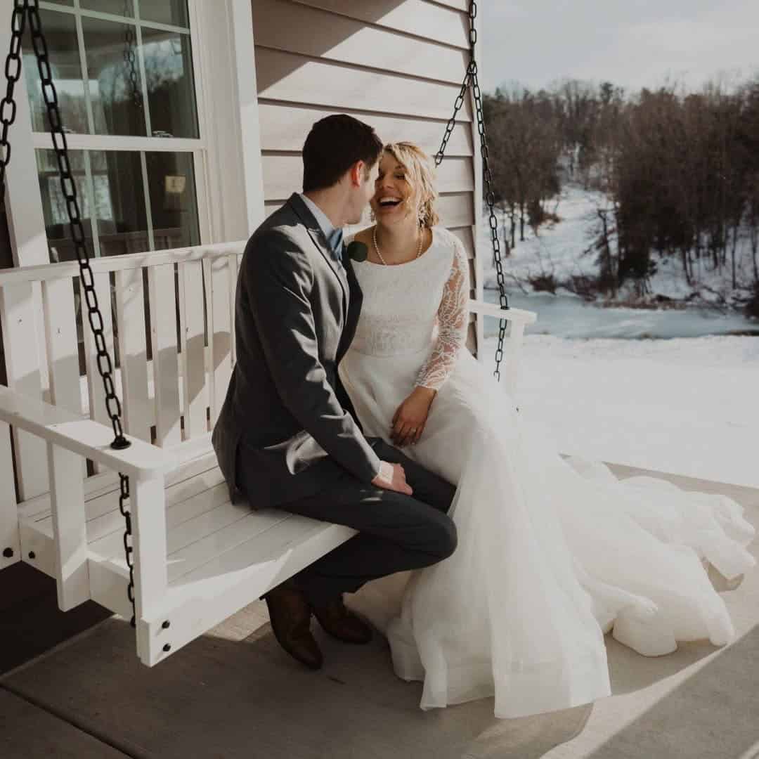 Just married couple sitting on porch swing in winter at Canaan Springs wedding venue in Northern Virginia near Winchester, VA, snow-covered farmhouse