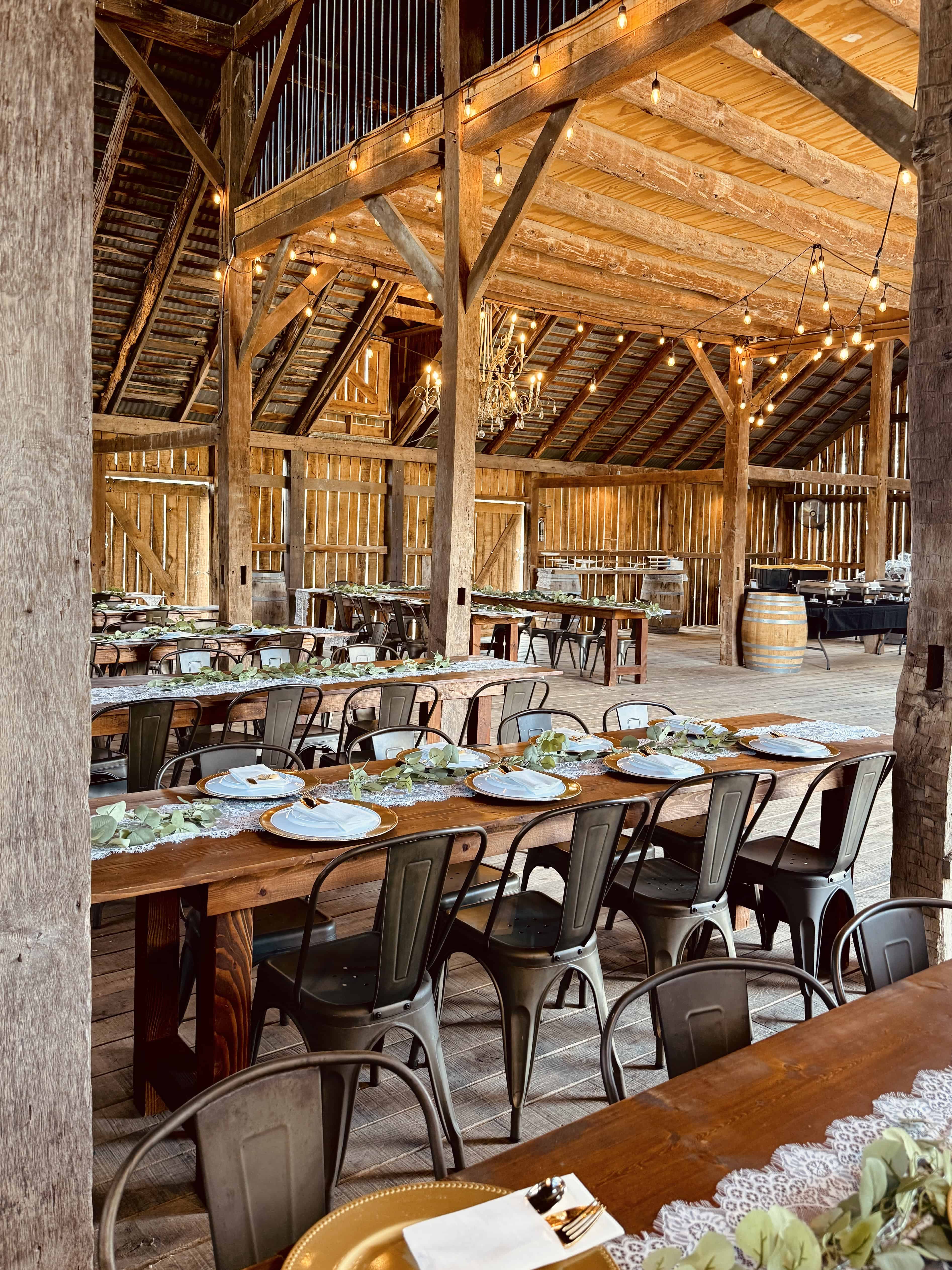 Wedding reception setup inside the historic barn at Canaan Springs near Winchester, Virginia, showcasing included farm tables, chairs, and chandeliers