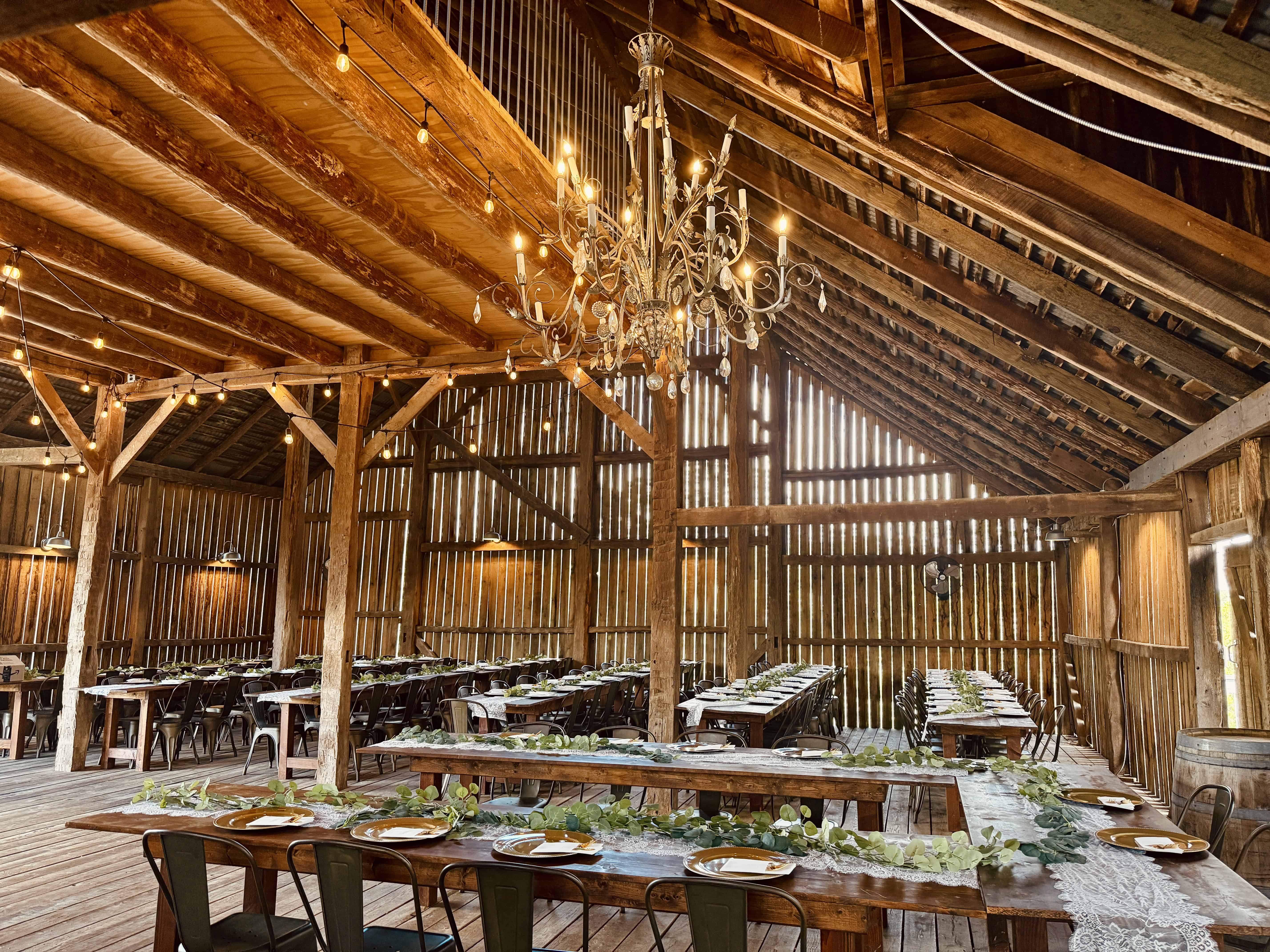Inside the historic barn wedding venue at Canaan Springs near Winchester, Virginia, featuring chandeliers, farm tables, and an elegant reception setup