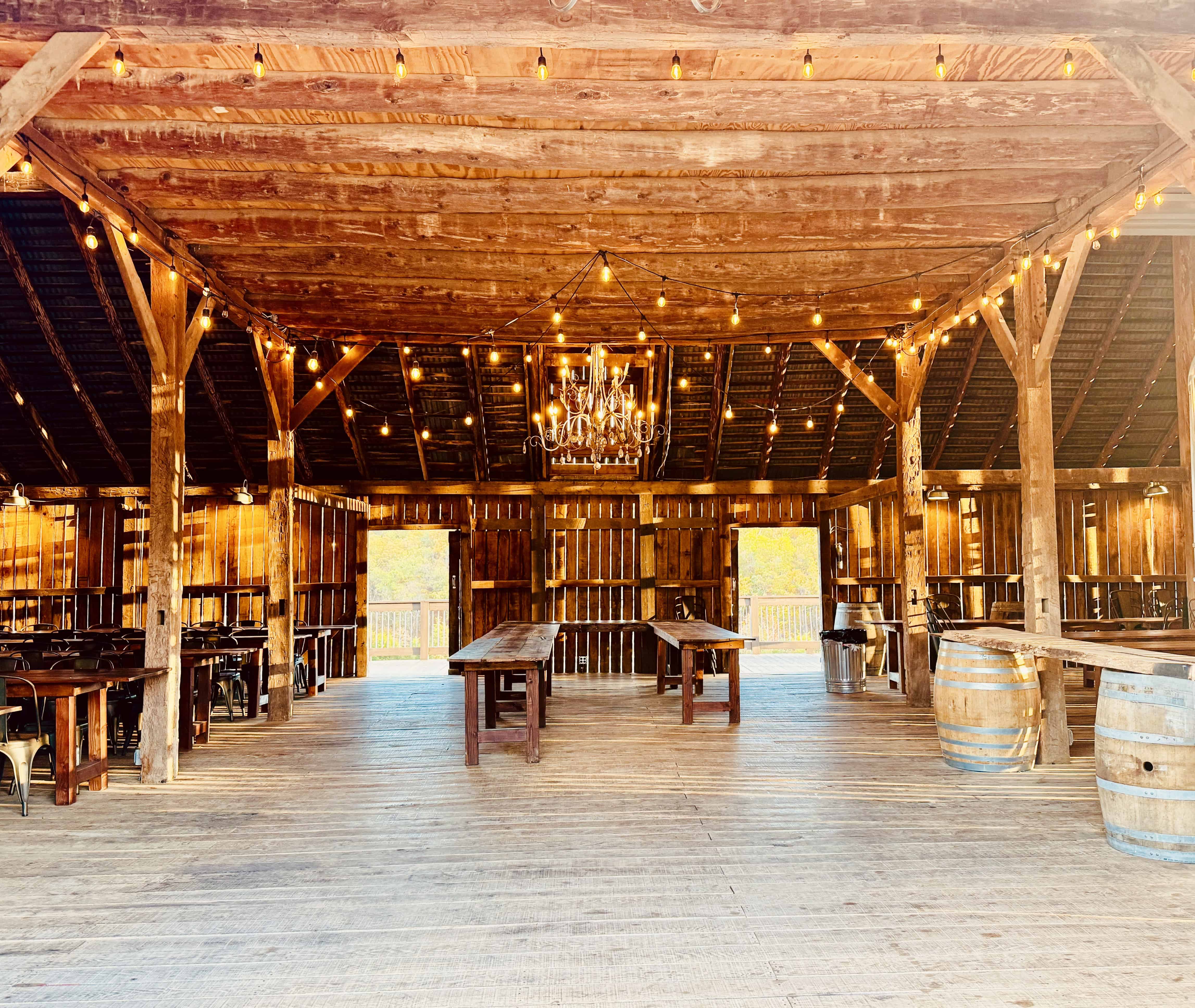 Undecorated barn interior with farm tables, chairs, barrels, and chandelier at Canaan Springs, a Northern Virginia barn wedding venue near Winchester, VA
