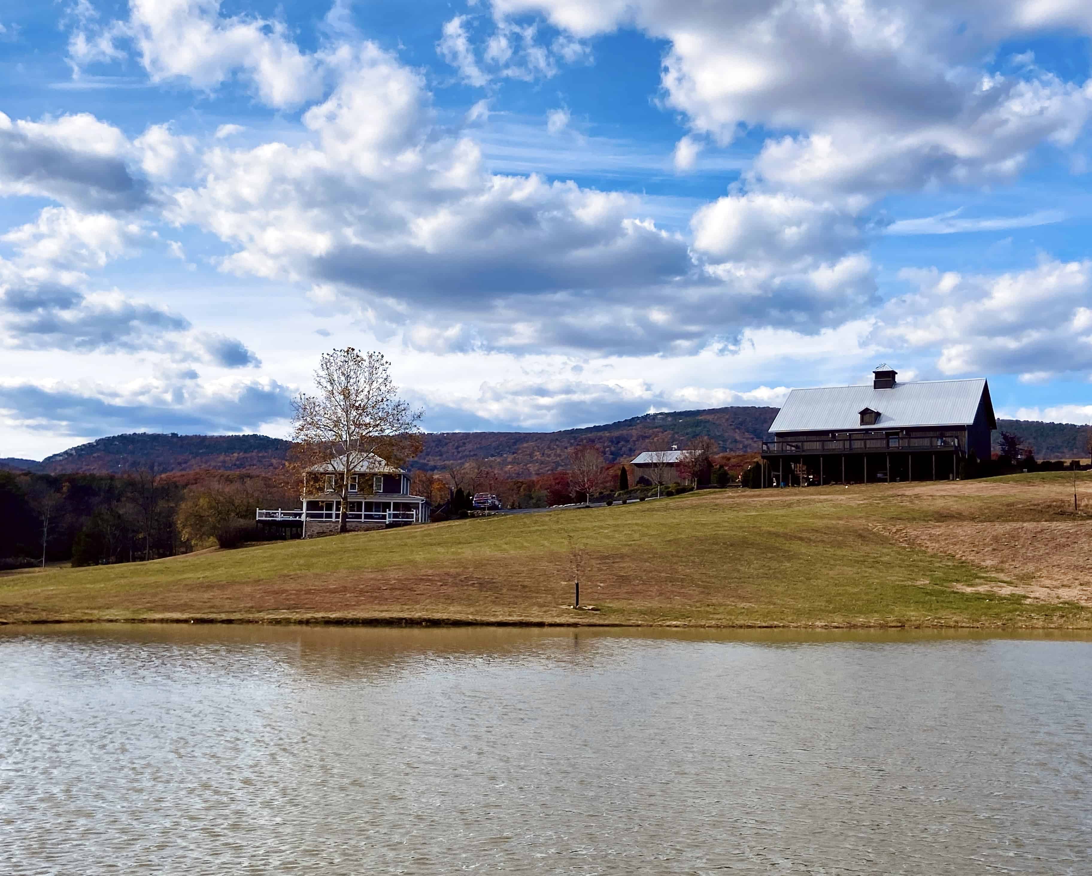 Wide view of Canaan Springs Northern Virginia wedding venue in fall, showing the pond in the foreground with warm autumn skies, historic barn, and farmhouse in the background near Winchester, VA.