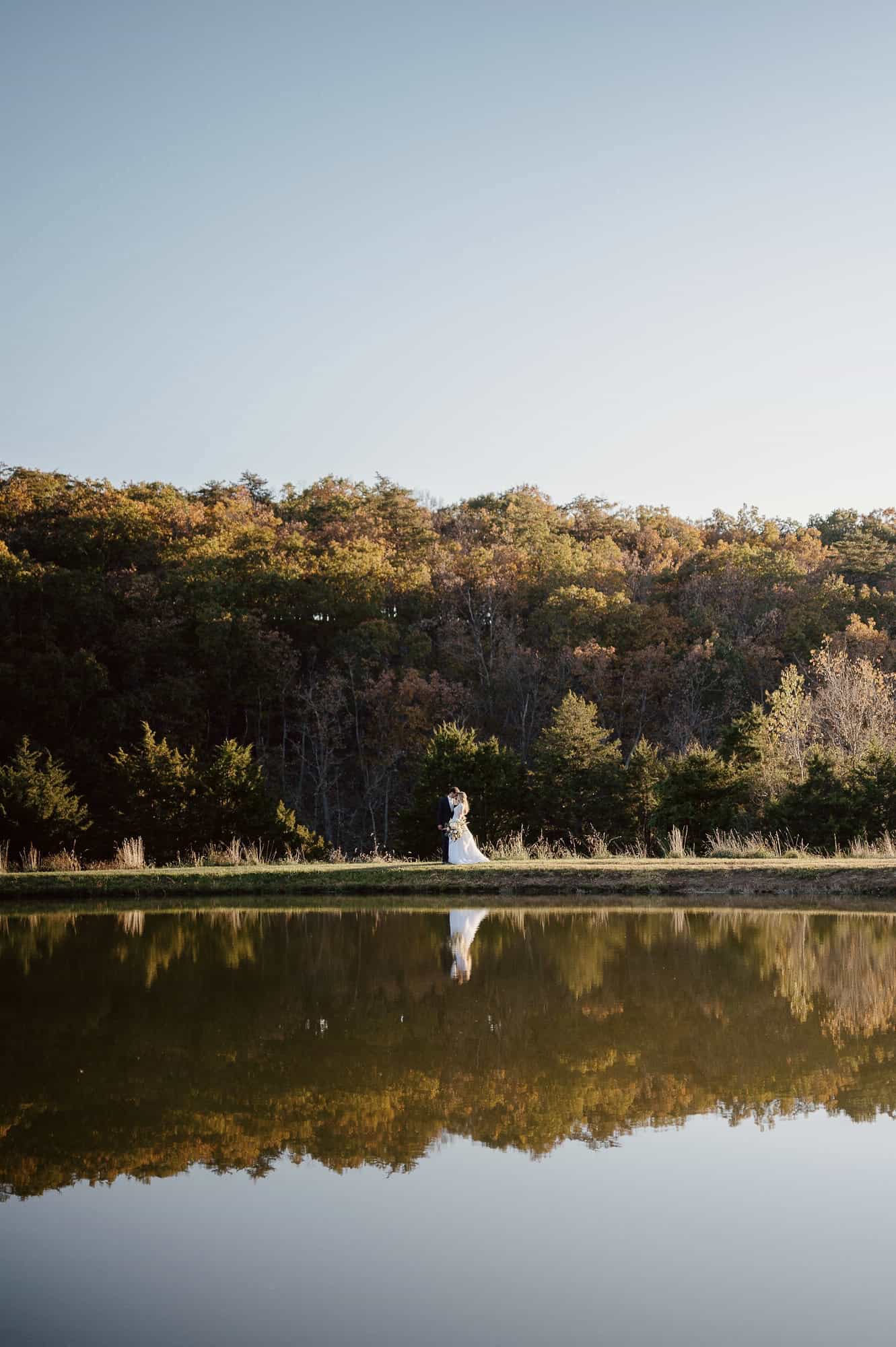 Just married couple reflected in a large pond at Canaan Springs Northern Virginia wedding venue near Winchester, Virginia, featuring expansive farm landscape and scenic water views.