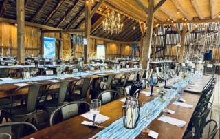 Elegant wedding reception inside the historic barn at Canaan Springs, a Northern VA barn wedding venue near Winchester, featuring farmhouse tables, metal chairs, chandeliers, string lights, and blue table runners.